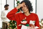 A tired looking woman wearing a red holiday sweater rubs the bridge of her nose.