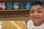 Male child sitting at a desk in a classroom with numbers behind him.