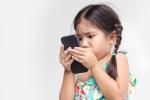 A young girl, with pigtails and wearing a green and yellow sundress, stares closely at a smart phone.