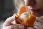 a woman holds a half-peeled mandarin close to her nose