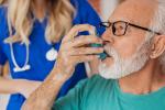 Man wearing green shirt breathing with inhaler with nurse standing behind him