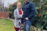Man and woman with grey and black dog in front of large tree