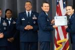 Shania Bennett stands next to four of her blue-uniformed Air Force superiors, and handed an award certificate by one of them