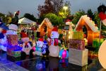 A row of colorful holiday inflatable snowmen, penguins, polar bears and gingerbread houses line a parking lot on a rainy evening