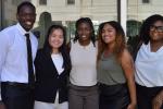 A group of five college students, all MINDGAP scholars, stand outside for a group photo next to a building lined with windows.