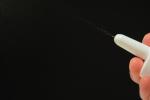 Close-up of a hand using a nasal spray device, with a fine mist spraying from the nozzle against a dark background.