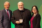 Kenneth W. Kizer is holding a medal in his hand and standing between Victor Dzau and Elena Fuentes-Afflick. 