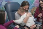 An adult sits in a medical chair with a child on their lap as a nurse begins a blood draw procedure and a second provider stands nearby.