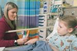 Woman holds markers as child lays in hospital bed smiling