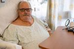 Man sitting in chair wearing hospital gown and scar down his chest