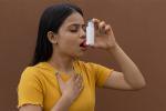 Woman taking deep breath and holding an inhaler to her mouth.