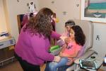 A child life specialist shows a father whose young daughter is sitting on his lap, how to hold her comfortably to receive a flu shot.