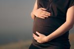 A woman wearing a short-sleeved black shirt cradles her pregnant stomach. She is visible from the top of her thighs to the shoulders. 