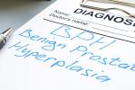 A clipboard holding white paper and the terms “diagnosis, Benign prostatic hyperplasia” with a silver pen, packet of yellow pills and two large books