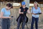In a field, three adults set up audio and video equipment to monitor wildlife. 
