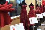 Five red dresses are displayed on mannequins and a bunch of red balloons in the background.