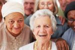 A diverse group of older people are gathered closely together and looking toward the camera and smiling.