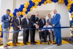 Seven men stand under a balloon arch at a ribbon cutting ceremony.