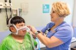 Child with green shirt being fitted with oxygen mask by respiratory therapist. 