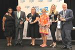 Six people stand on stage holding awards at convention.