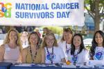 Six women sit under a sign that reads National Cancer Survivors Day