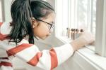 a young girl lines up wooden toys along a windowsill