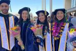 Four graduates posing and holding flower bouquets