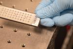 A gloved hand holds a plate for a mass spectrometer.