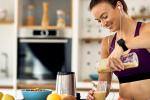 Sportswoman in workout clothes pouring a fruit smoothie in the kitchen