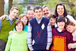 A group of 10 people poses outside for a group photo. Some have Down syndrome or other disabilities. Many have arms around each other. 
