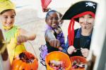 Three children trick-or-treating holding their containers out 