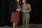 Two women stand next to each other holding glass awards.