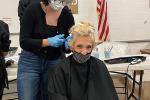 A woman seated with a black beauty salon cape gets her hair cut from a hairdresser standing behind her