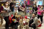 Eight people and two facility dogs pose in storeroom filled with toy donations