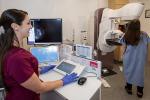 Woman in a red uniform assisting a patient during a mammogram in a medical imaging room.