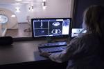 : Woman looking at monitor with images in front of room featuring large scanner in background.