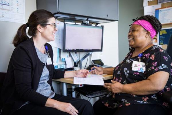 A nurse speaking to a PMHNP student in an office in front of a computer