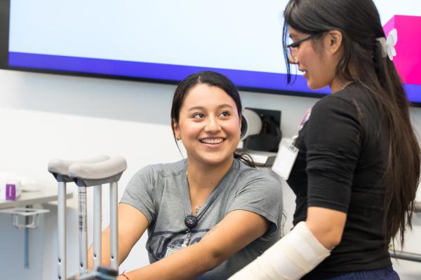 two students smiling at each other as one wears a cast on their arm