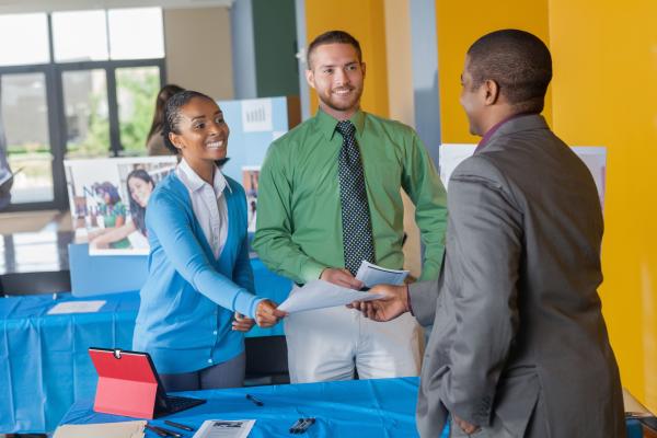 two people at a career fair handing information to a recruiter