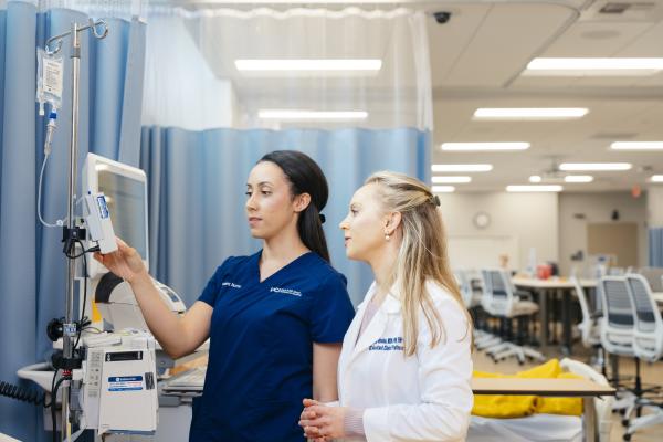 UC health professional student and an instructor standing together and looking at an IV in a learning simulation lab