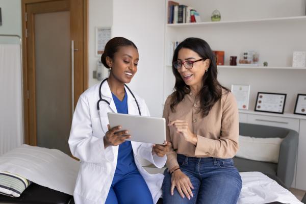 A healthcare provider in a white coat sitting next to a patient looking at a screen