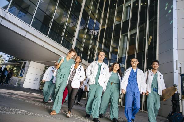 Image showing UC medical school students dressed in scrubs and white coats walking in front of a hospital building. Text on photo says Applying to UC medical schools