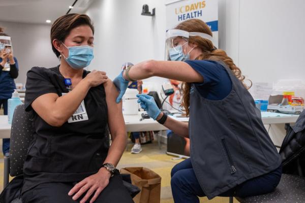 Woman wearing scrubs with sleeve rolled up and receiving injection in arm