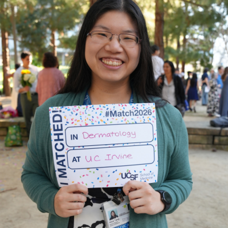 photo of Alice Tang smiling and holding a "I matched!" sign outside 