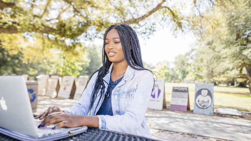 UC student works from a laptop outside on campus