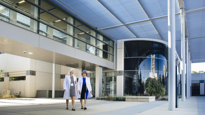 Exterior of a UC hospital with two medical professionals walking