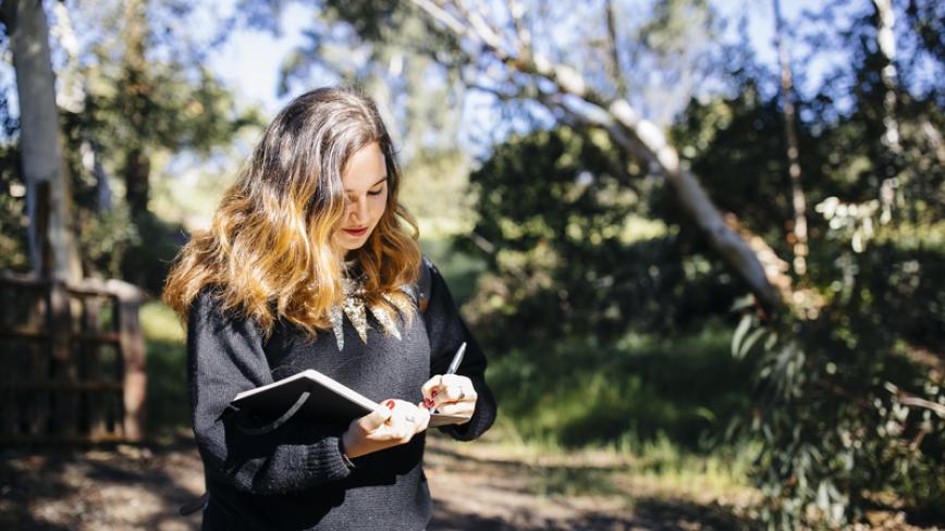Photo of woman taking notes in a notebook surrounded by trees