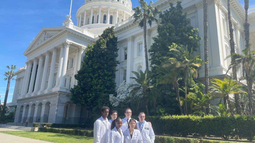 group of students and the dean in white coats outside that state captitol