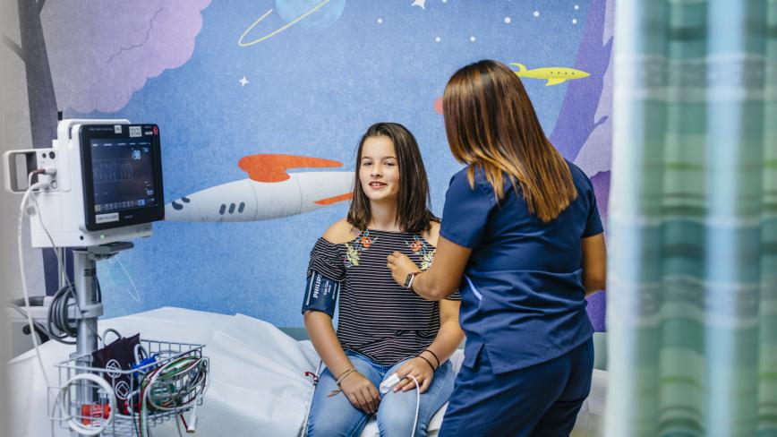 image of a health care professional in blue scrubs caring for a young person sitting down, with a mural in the background