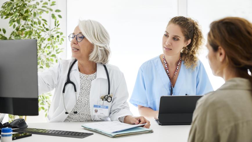 image of two health care professionals looking on a computer and talking to a patient